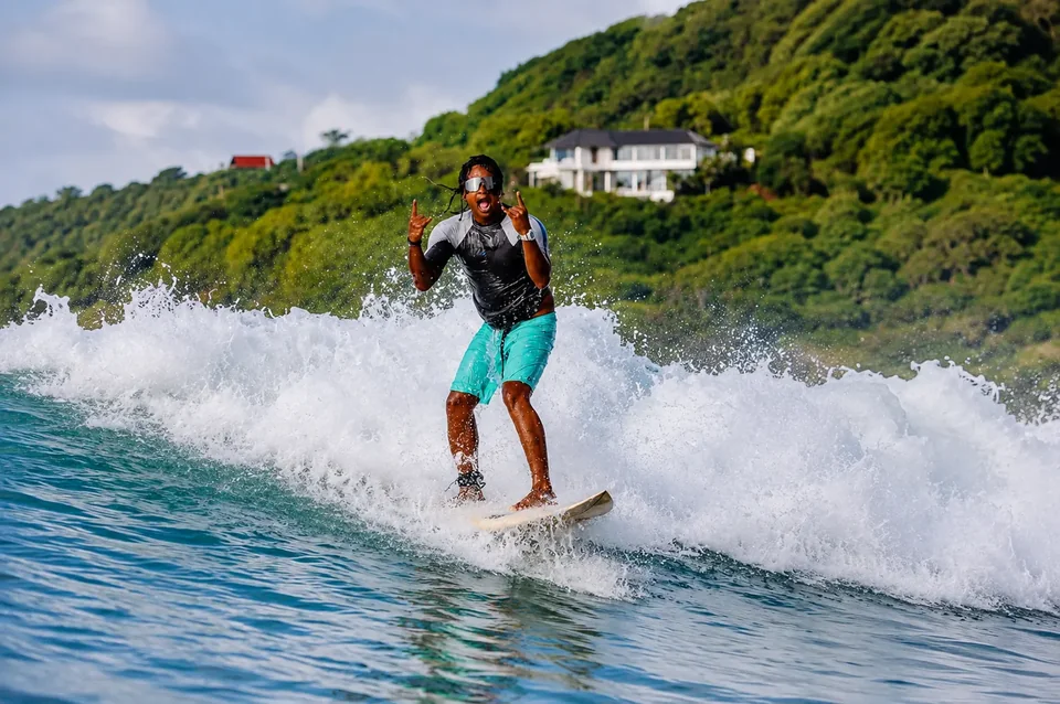 Pak Jumbo surfing a peeling wave in Gerupuk Bay with a shaka hand sign
